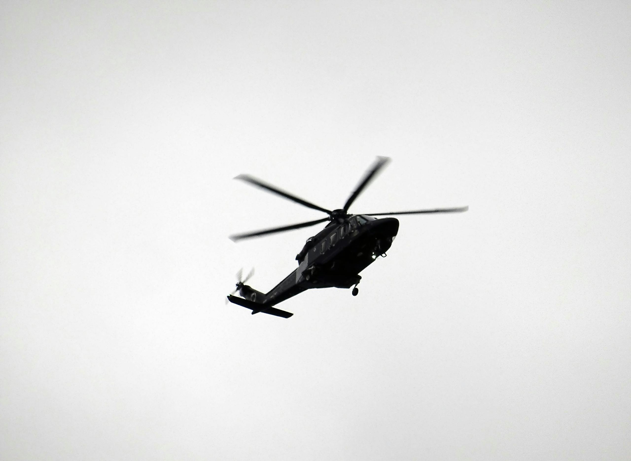 A black helicopter silhouetted against an overcast sky in a monochrome image, capturing a sense of flight and aviation.