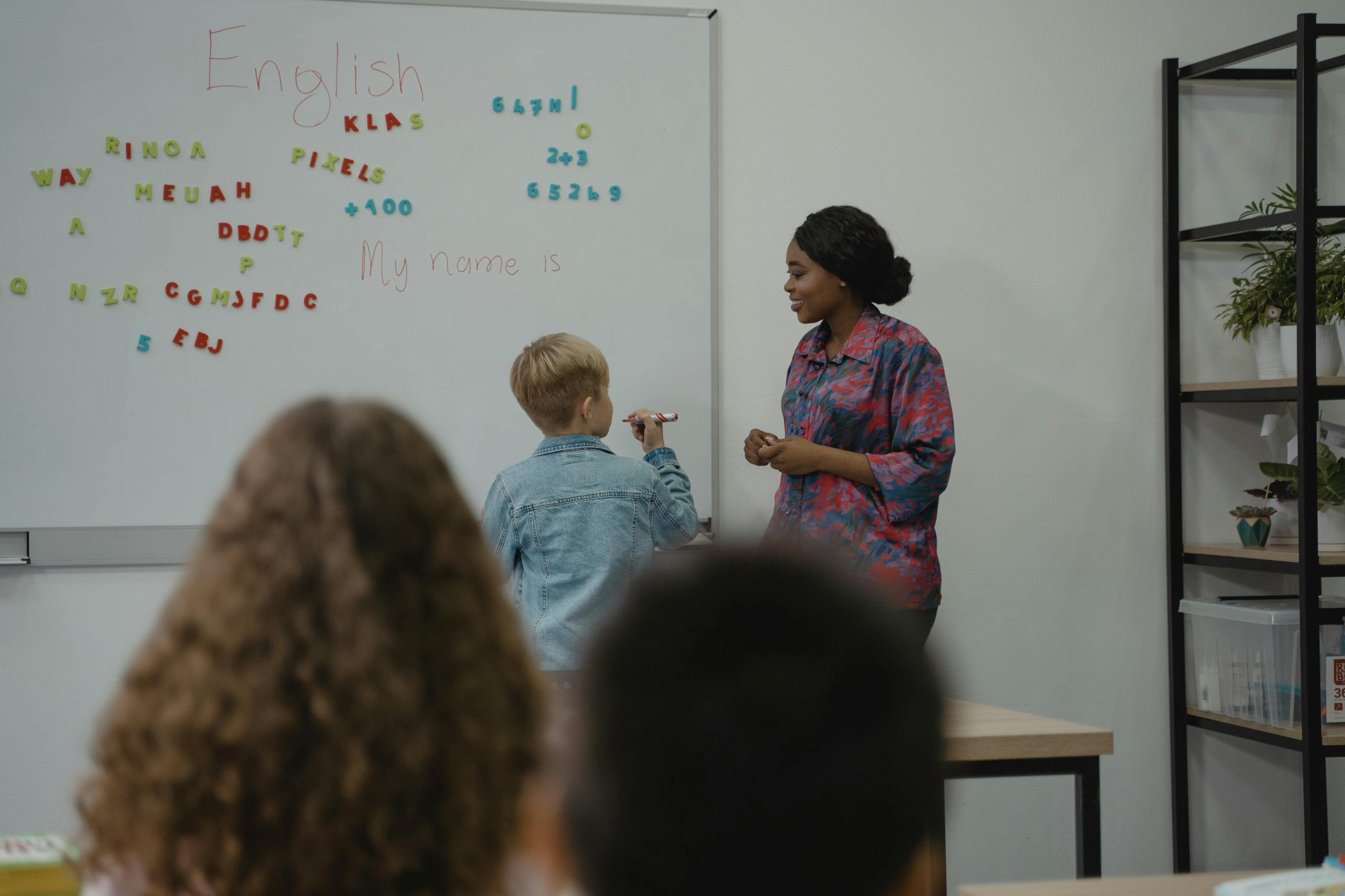 A teacher engages students in an interactive English lesson using a whiteboard and magnetic letters.