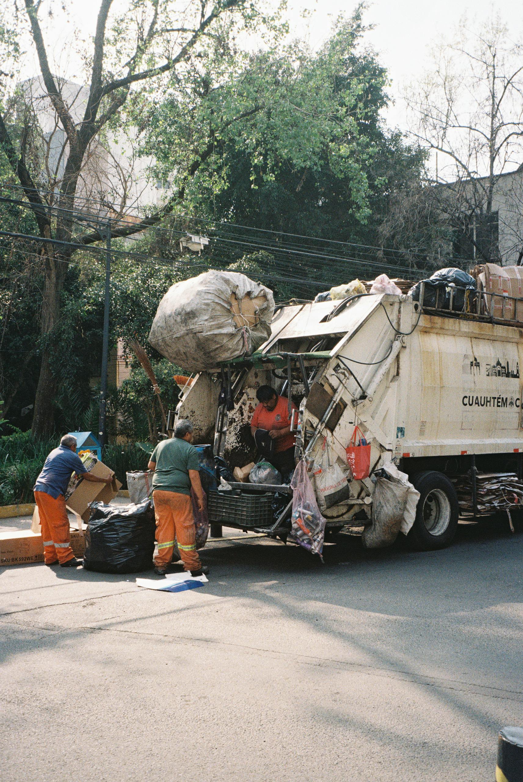 Street workers in Mexico City loading garbage truck during daytime.