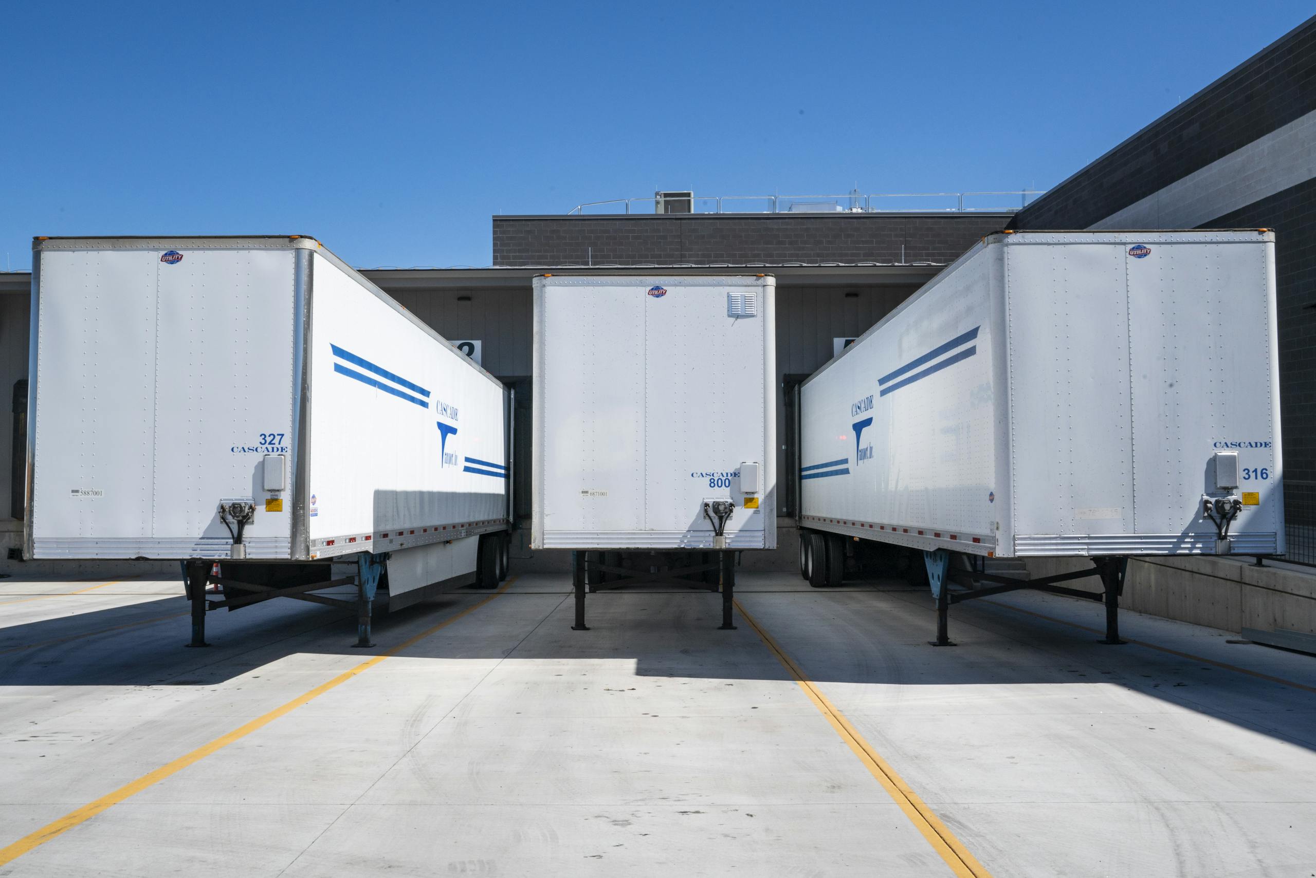 Three white cargo trailers parked at an industrial shipping dock under clear blue skies.